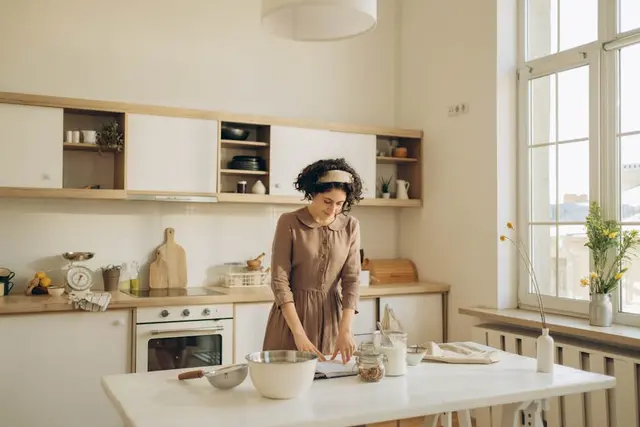 A woman with curly hair prepares food in a bright and cozy home kitchen, embracing a peaceful lifestyle.